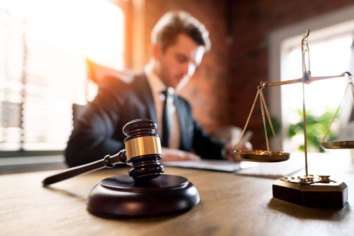 Male attorney writing at desk with gavel and scales of justice