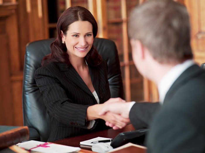 Brunette businesswoman sitting in leather chair shaking hands with man.