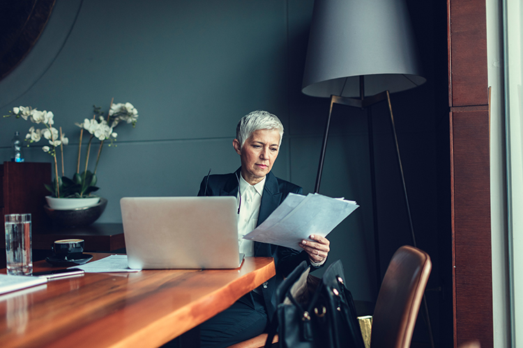 Woman with silver hair sits at a table reviewing law firm malpractice insurance coverage documents, with her laptop open