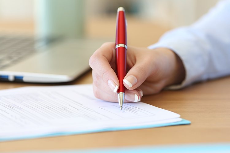 A woman with light skin writing on a piece of paper.