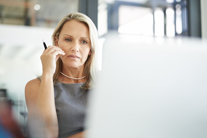 A female lawyer contemplates while looking at a computer screen as she works on her firm’s risk management strategy.